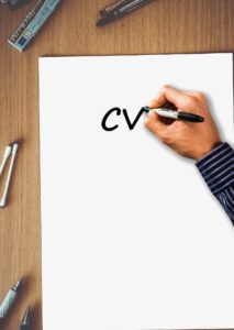 A hand writes the letters "CV' on a blank piece of paper. 